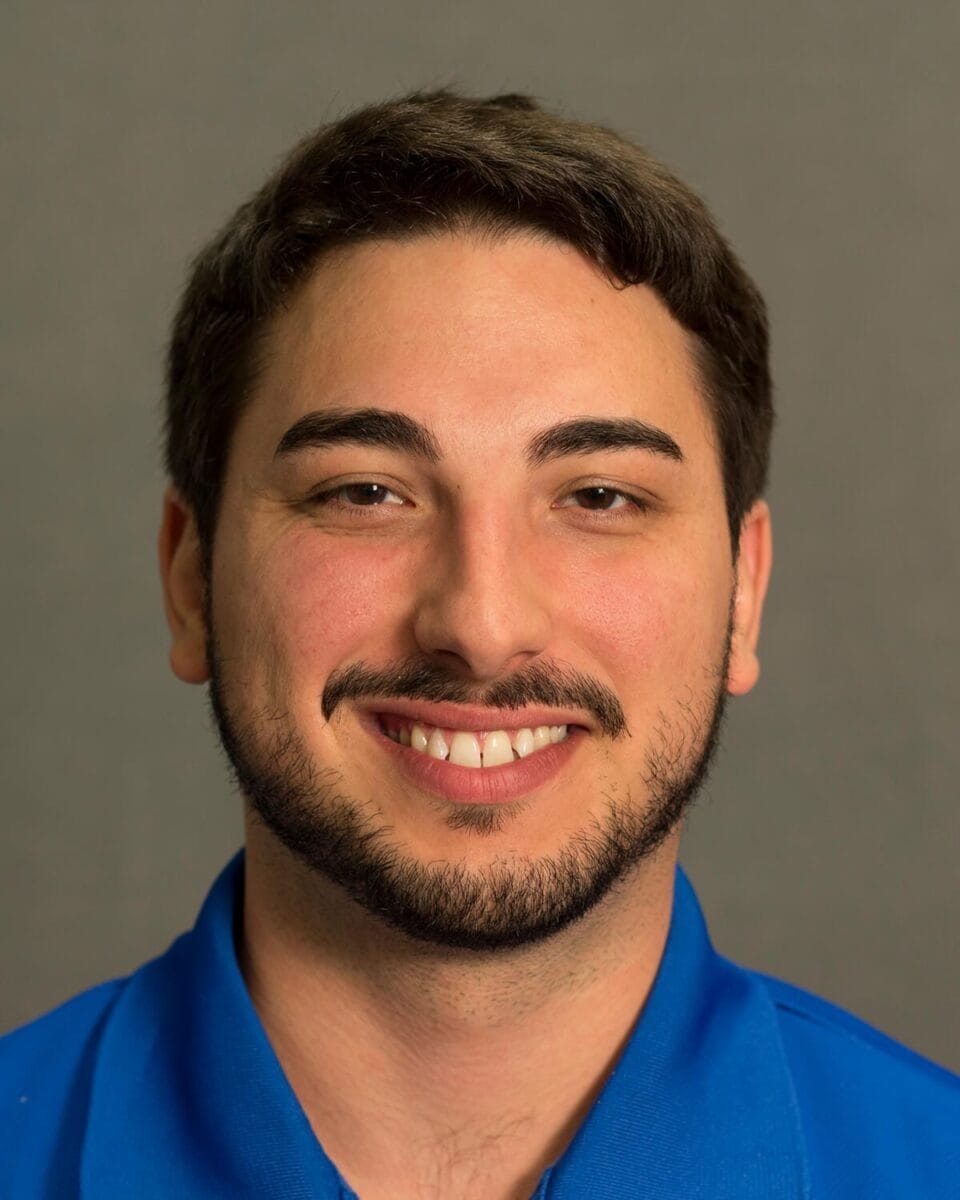 Thomas Tkach ACC headshot photo, smiling man wearing a blue shirt in front of neutral background