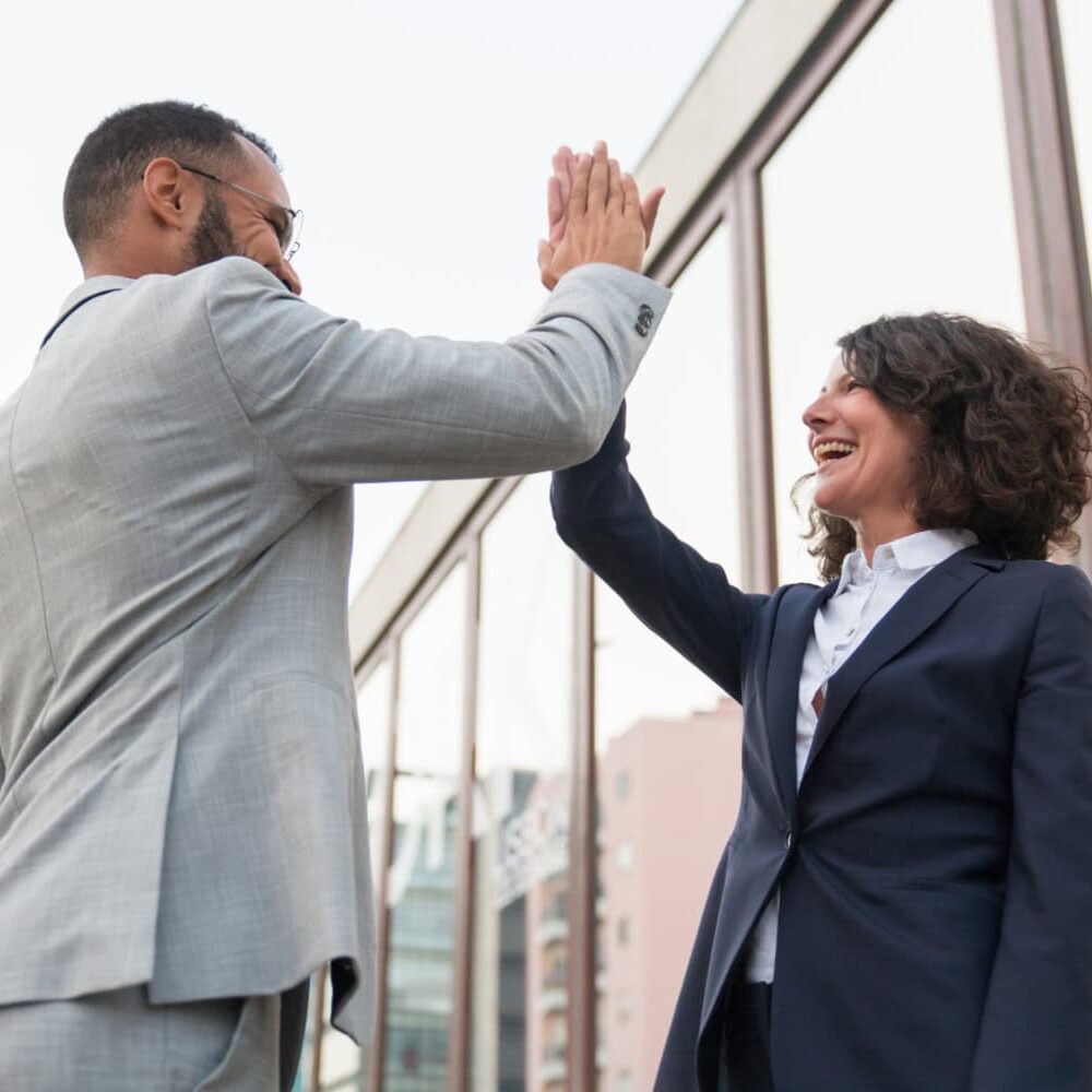 A man and woman high five each other in an outdoor city landscape celebrating their investment in their growth