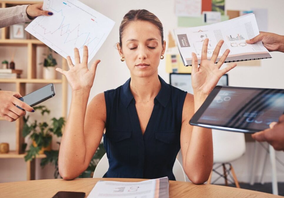 woman with eyes closed holding up her hands seemingly saying no to many other hands with phone tablet and papers around her head