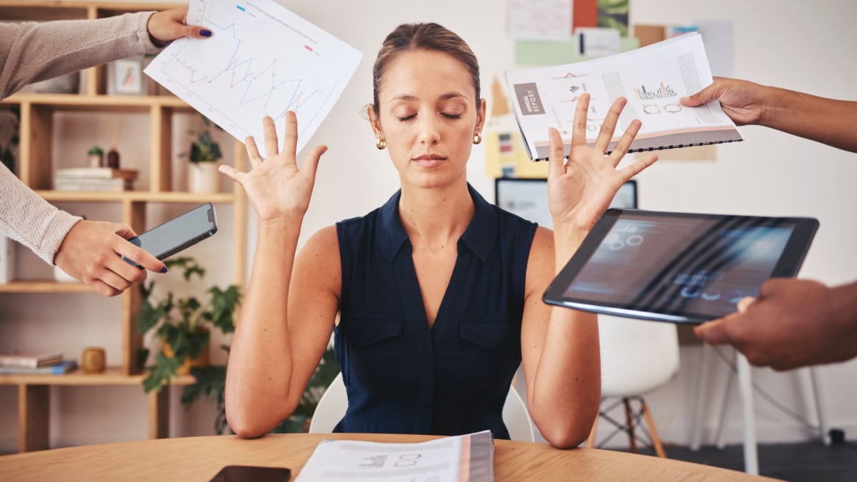 woman with eyes closed holding up her hands seemingly saying no to many other hands with phone tablet and papers around her head