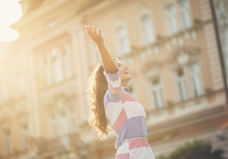 woman holding arms up in joy in front of a building