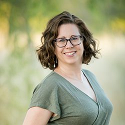 Angela Lindley PCC headshot photo, brown haired smiling woman in a green top outside
