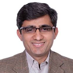 Dr Badrei Bajaj PCC headshot photo, dark haired smiling man with glasses in tan blazer against white background