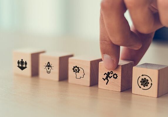 wooden blocks lined up evenly on a table with icons on each and a person touching a block with the icon on a running person with two gears