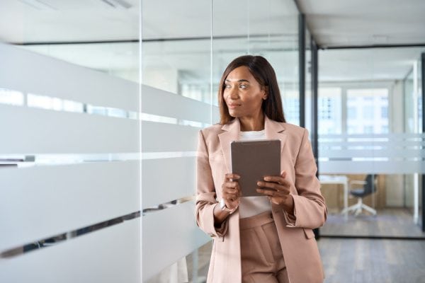 coach leaning against glass wall with tablet looking through wall and smiling