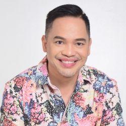 Myke Celis PCC MA headshot photo, smiling man with dark hair in a floral shirt in front of a white background