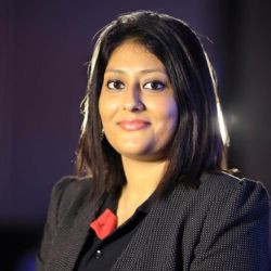 Amrita Choudhury ACC headshot photo, dark haired woman wearing dark top against dark background smiling