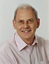 David Clutterbuck headshot photo, smiling man wearing glasses and a collared shirt in front of white background