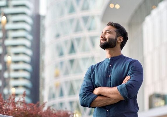 smiling coach with arms crossed outside of some buildings