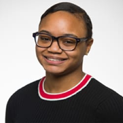 Ezraya Drumgo headshot photo, smiling woman wearing glasses and red white black sweater in front of a white background
