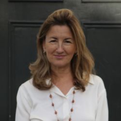Tiffany Gaskell headshot photo, smiling woman with light brown hair wearing white collared shirt in front of dark door