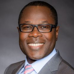 Fred Gatty headshot, man with dark hair glasses suit and tie smiling