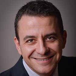 George Bragadireanu MCC headshot photo, dark haired man in black blazer smiling