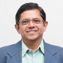 Hemant Deshpande PCC headshot photo, smiling man in gray blazer and light green collared shirt wearing glasses