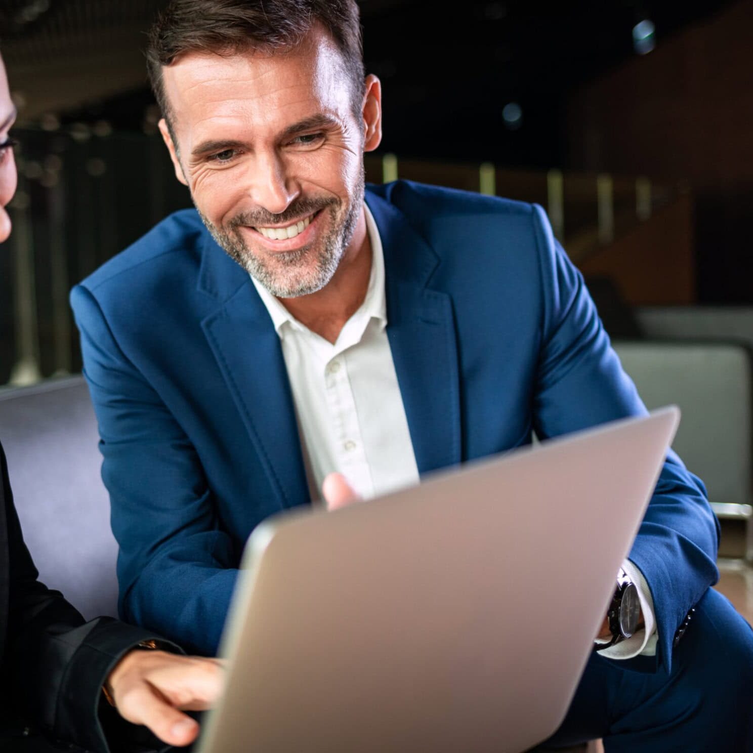 Male and female professionals smiling and working on a laptop during a coaching session, focusing on leadership development and career growth.