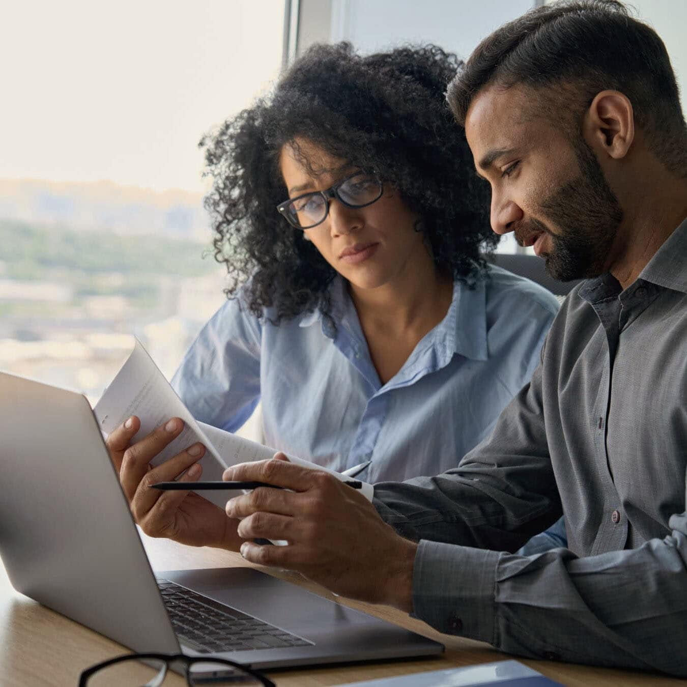 A man and woman review information on a computer screen in a casual office.