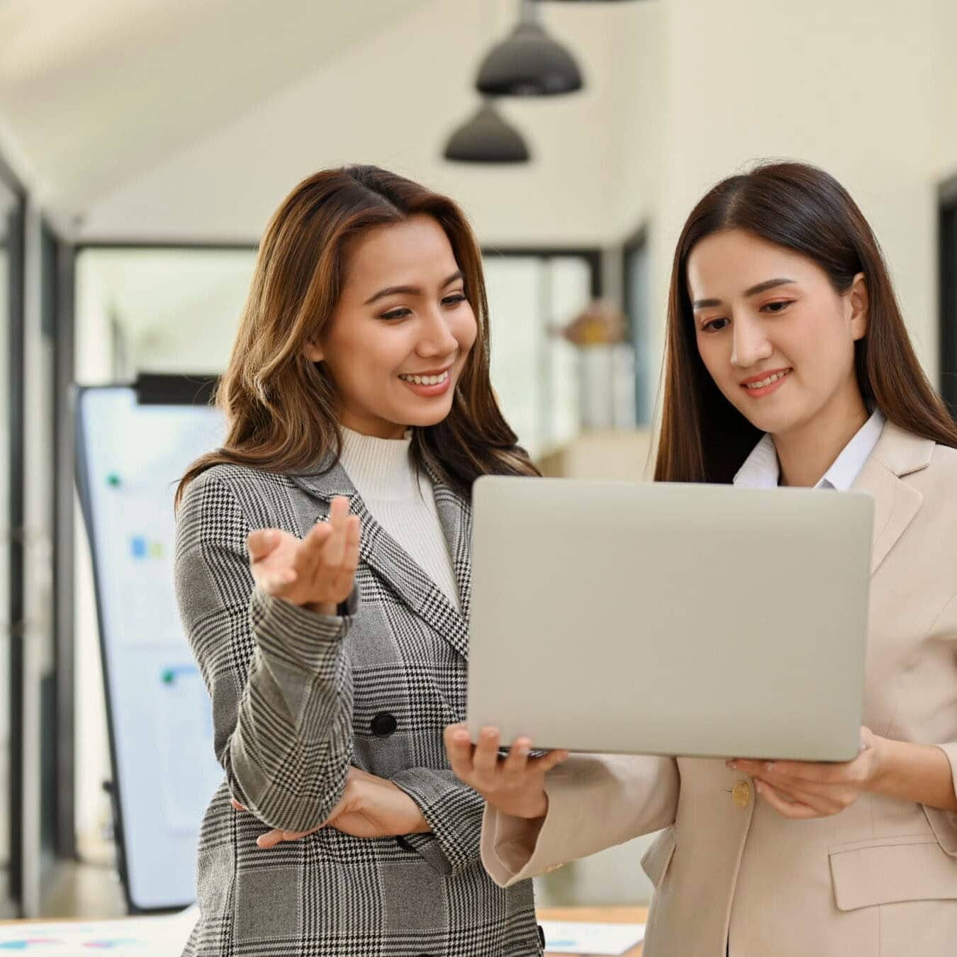 Two woman look at the computer while in an office setting.