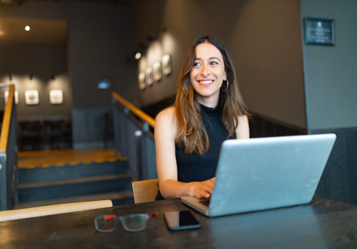 Young, Caucasian woman working on a laptop. Blurred background portrays a professional space and staircase.