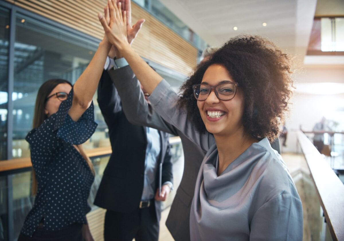 Cheerful African-American office worker giving high five to colleagues and looking at camera.