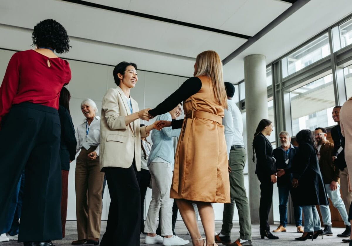 Two diverse women holding hands and smiling during a professional networking event, symbolizing mentorship, inclusion, and belonging in the International Coaching Federation community.