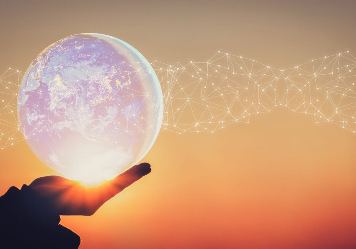 A hand gently holding a translucent white globe with white interconnected lines and dots radiating outward, set against a warm gradient background shifting from brown to yellow, orange, and red. Together, these elements convey a powerful message of global impact, interconnectedness, and forward-looking leadership.