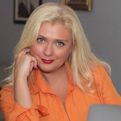 Dr Inna Post ACC headshot photo, blond smiling woman with orange top in and office