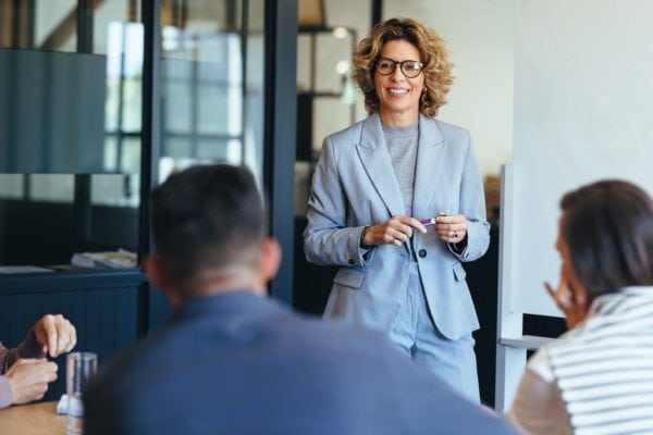 woman in a conference room looking confident and speaking to a group of business professionals seated at the table