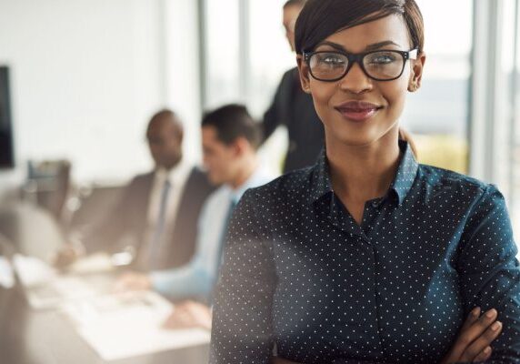 smiling woman with people meeting at a conference table behind her