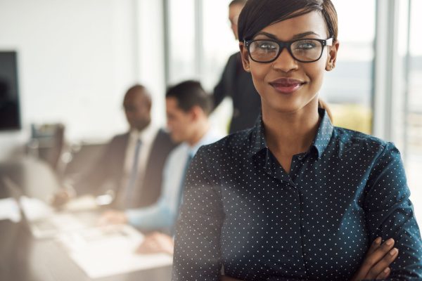 smiling woman with people meeting at a conference table behind her