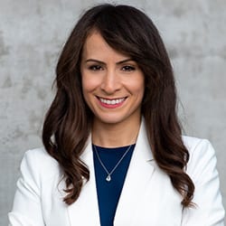 Lisa Christen PCC headshot photo, smiling woman with brown hair wearing a white blazer and blue top in front of gray background