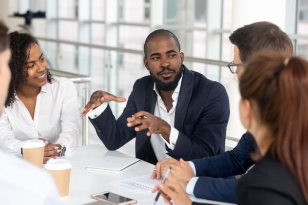 man talking to business peers at a table with all of them listening intently