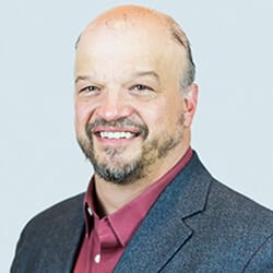 Michael Marx MCC headshot photo, smiling man with gray blazer and maroon collared shirt in front of light background