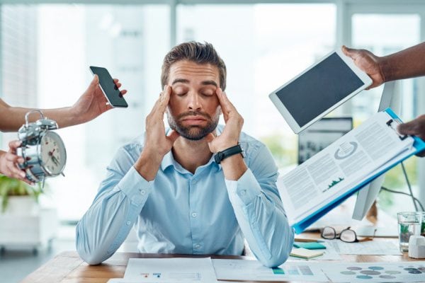 man looking stressed with hands on face and eyes closed, surrounded by various objects signifying demands and responsibilities