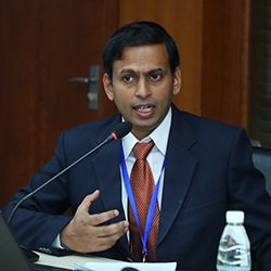 P Venkatesh ACC headshot photo, dark haired man talking on a microphone to unseen listener