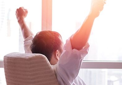 seated male in front of a window raising arms up in victory