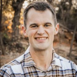 Brady Ross ACC headshot photo, man outside in a plaid button up shirt smiling