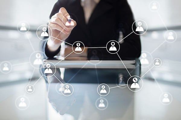 woman at table using pen to connect people icons on transparent screen