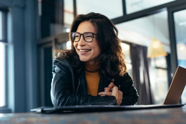 smiling woman looking to her right while sitting at a table with her laptop
