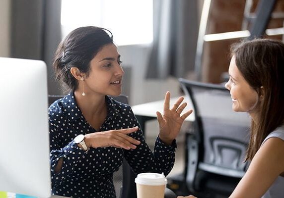 coach and client talking in front of a computer and one has a coffee cup