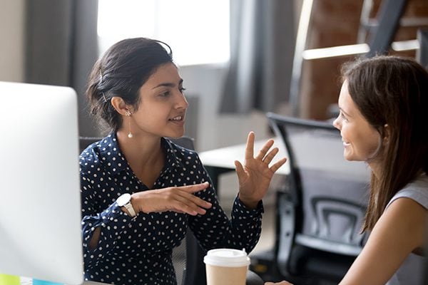 coach and client talking in front of a computer and one has a coffee cup