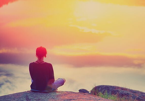 woman sitting on the edge of a mountain looking out at a sunrise