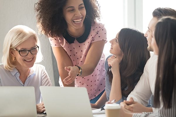 five people meeting and engaged in conversation in front of two laptops