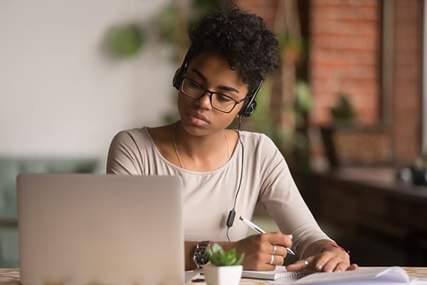 woman listening to audio from a laptop and taking notes