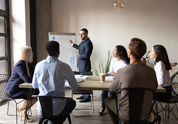 coach using large note pad or white board to lead a group of professionals at a table