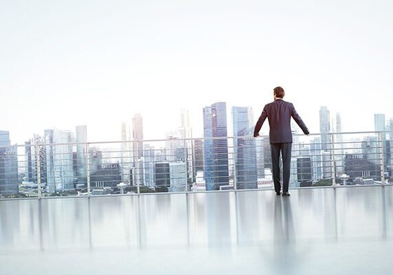 man standing at the railing of a highrise building overlooking a city