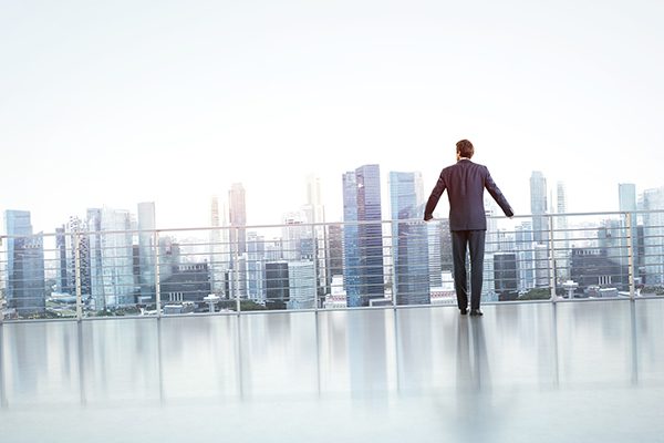 man standing at the railing of a highrise building overlooking a city