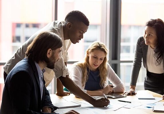 four people meeting around a table with one making marks on a piece of paper