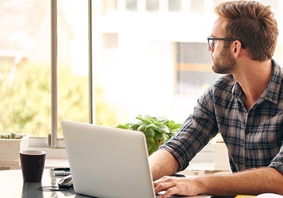 coach procrastinating by looking out of a window while his hands are on a laptop keyboard