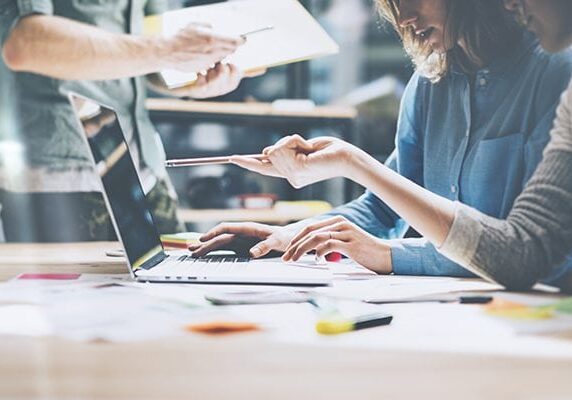 three people meeting around a laptop and one pointing to the screen