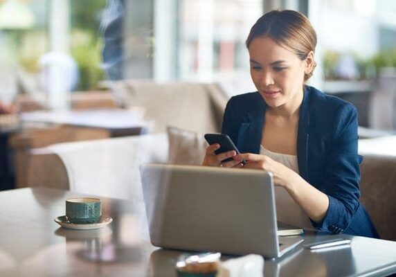 woman distracted on her cellphone sitting in front of her laptop